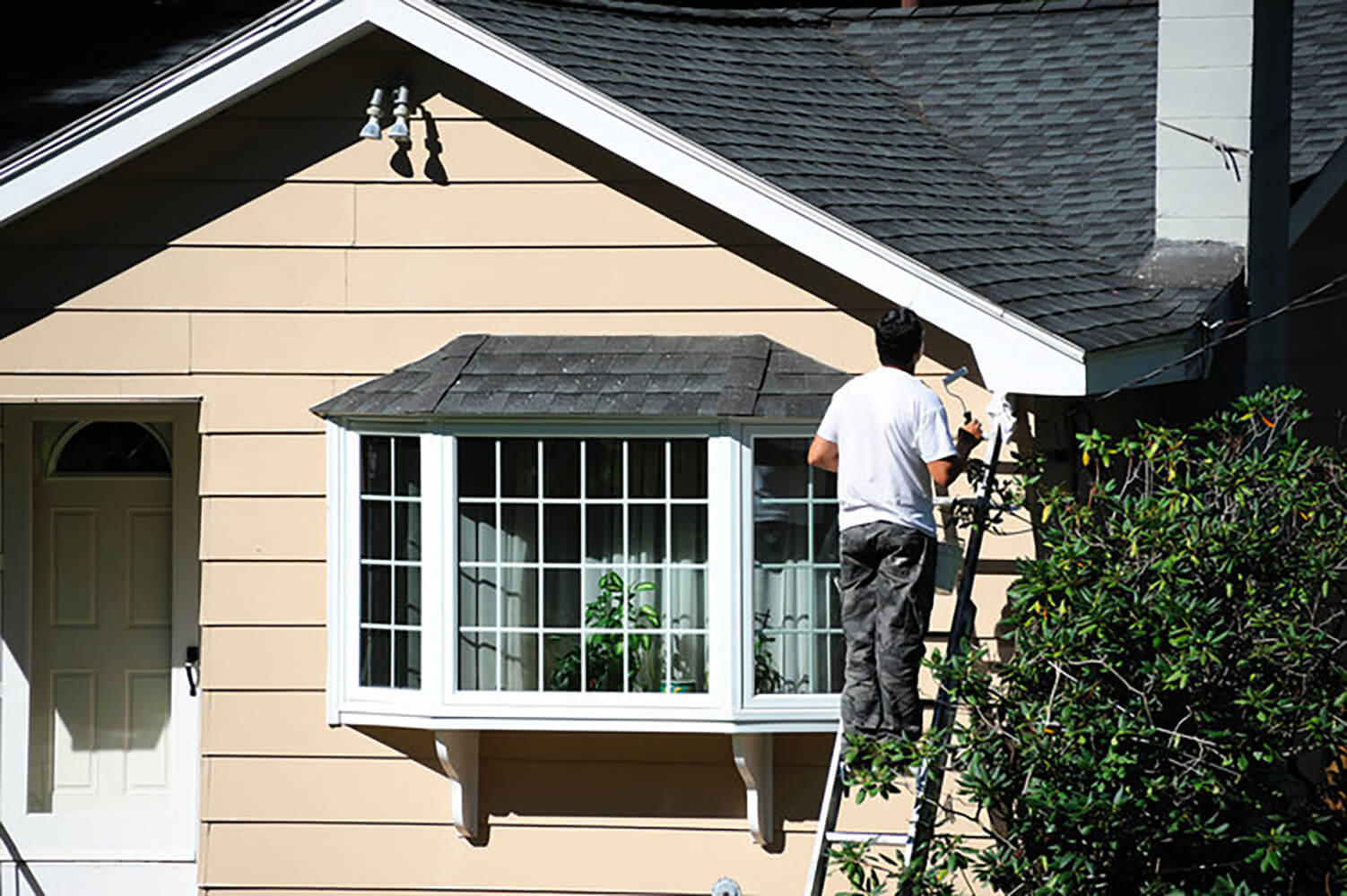A painter on a ladder painting the exterior of a home during the best time for exterior house painting.